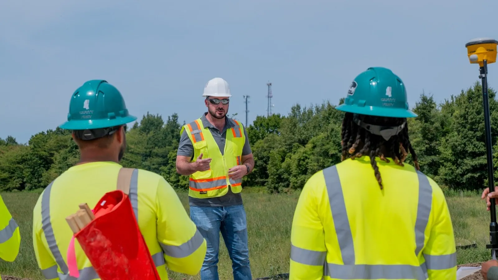 A construction crew in hard hats and safety vests gathered on a job site